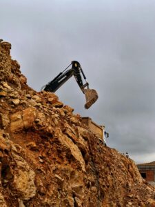 Solid Minerals Extraction A construction excavator moving rocks at a quarry, captured under cloudy skies.